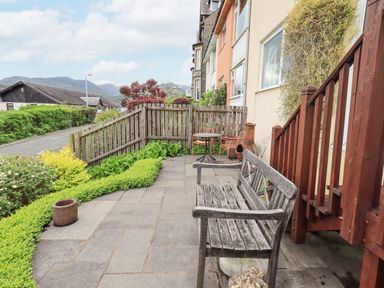 A garden patio with a wooden bench table and chairs beside a wooden fence at Fellcroft in Troutbeck