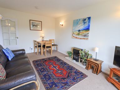 A living room with a leather sofa a wooden dining table with chairs a patterned rug and a fireplace at Fellcroft in Troutbeck