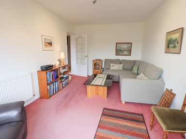 A living room with a gray sofa coffee table bookshelf and paintings at Fellcroft in Troutbeck