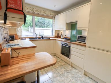A kitchen with wooden countertops white cabinets sink oven microwave and a window overlooking a garden at Fellcroft in Troutbeck