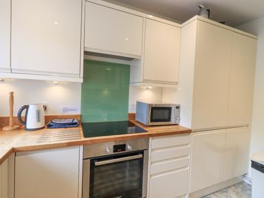 A kitchen with white cabinets a wooden countertop an electric stove an oven a microwave and a kettle at Fellcroft in Troutbeck