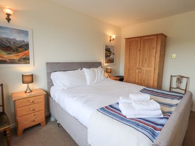 A bedroom with a double bed white bedding wooden wardrobes bedside tables with lamps and framed pictures on walls at Fellcroft in Troutbeck