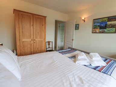 A bedroom with a bed with folded towels a wooden wardrobe a chair and paintings on the wall at Fellcroft in Troutbeck