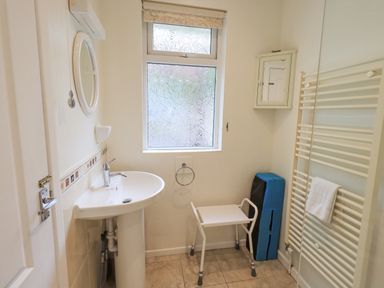 A bathroom with a sink a small white stool a towel radiator and a frosted window at Fellcroft in Troutbeck
