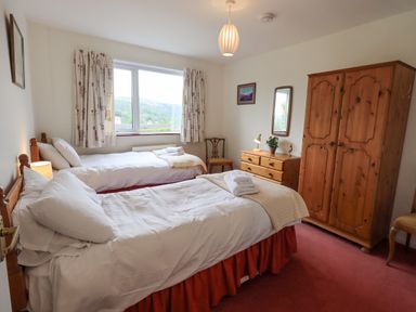 A bedroom with two single beds bedside table chest of drawers wardrobe and window with curtains at Fellcroft in Troutbeck
