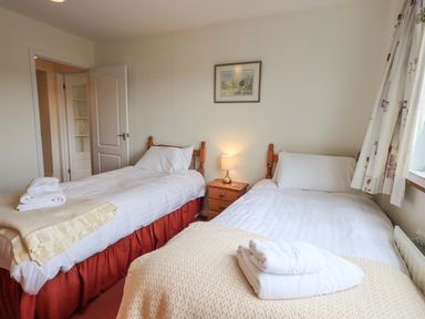 A bedroom with two single beds separated by a small wooden nightstand with a lamp at Fellcroft in Troutbeck