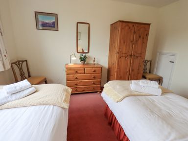 A bedroom with two single beds wooden dresser and wardrobe with chairs against the walls at Fellcroft in Troutbeck