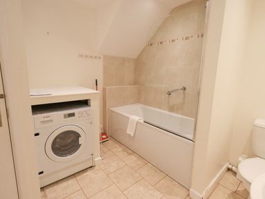A bathroom with a washing machine bathtub with glass shower screen and a toilet at Fellcroft in Troutbeck