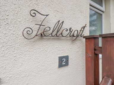 A wall with a metal sign saying Fellcroft and a house number 2 beside a wooden fence at Fellcroft in Troutbeck