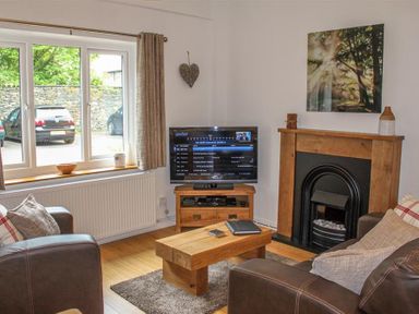 A living room with leather sofas a wooden coffee table television and a fireplace at Four Seasons Cottage in Ambleside