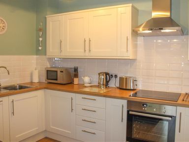 A kitchen with white cabinets stainless steel appliances and wooden countertops at Four Seasons Cottage in Ambleside