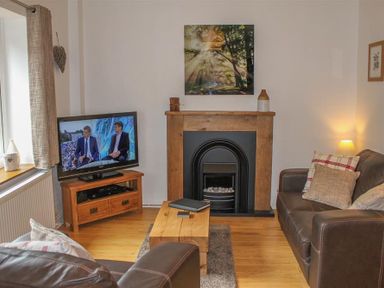 A living room with a television on a wooden stand a fireplace with a wooden mantel brown leather sofas and a wooden coffee table at Four Seasons Cottage in Ambleside