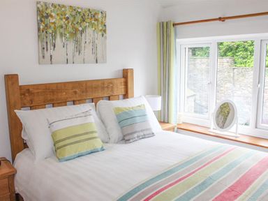 A bedroom with a wooden bed frame striped pillows and blanket a window with curtains and a mirror on the sill at Four Seasons Cottage in Ambleside