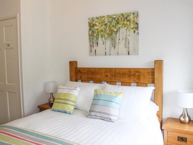 A bedroom with a wooden bed frame striped pillows and two bedside tables with lamps at Four Seasons Cottage Ambleside