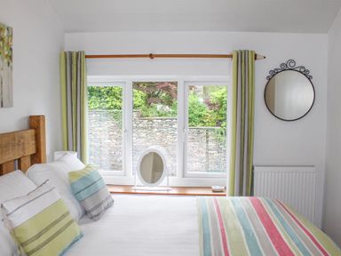 A bedroom with a wooden bed with striped pillows and blanket beside a window with curtains at Four Seasons Cottage in Ambleside