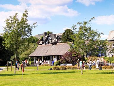A group of people walking and standing on a grassy area with trees near a thatched roof building at Four Seasons Cottage in Ambleside