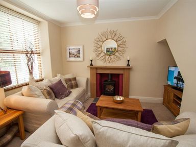 A living room with cream sofas a wooden coffee table and a fireplace at Acorn Cottage in Ambleside