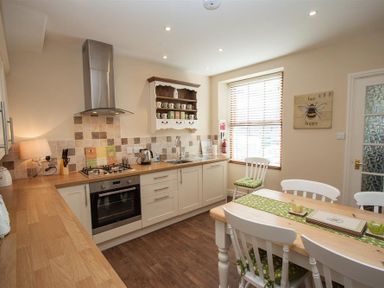 A kitchen with wooden countertops white cabinets a dining table with chairs and a window with blinds at Acorn Cottage in Ambleside