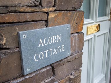 A stone wall with a plaque reading Acorn Cottage next to a door with a mail slot at Acorn Cottage in Ambleside