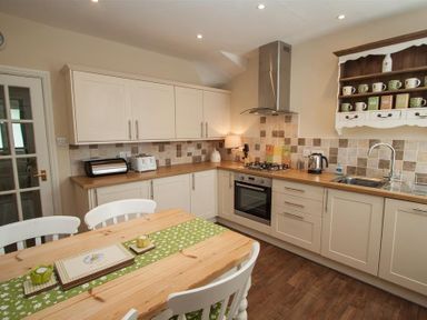 A kitchen with white cabinets wooden countertops a stove oven sink a wooden table with chairs and a green table runner at Acorn Cottage in Ambleside