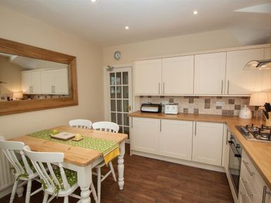 A kitchen with white cabinets wooden countertops and a wooden dining table with white chairs at Acorn Cottage in Ambleside