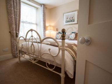 A bedroom with a decorative metal bed frame pillows patterned curtains and a floor lamp at Acorn Cottage in Ambleside