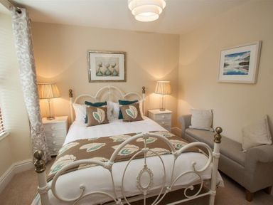 A bedroom with a metal bed frame two bedside tables with lamps a sofa and framed artwork at Acorn Cottage in Ambleside