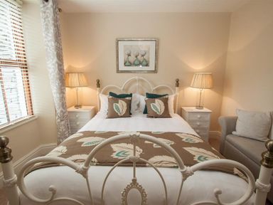 A bedroom with a white metal bed frame two bedside tables with lamps a gray sofa and a window with curtains at Acorn Cottage in Ambleside