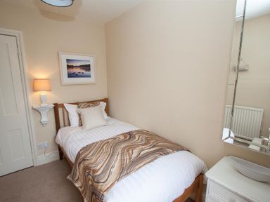 A small bedroom with a single bed a bedside lamp a framed picture a mirror and a small white dresser at Acorn Cottage in Ambleside