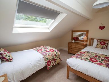 A bedroom with two single beds a wooden dresser and a skylight window at Acorn Cottage in Ambleside