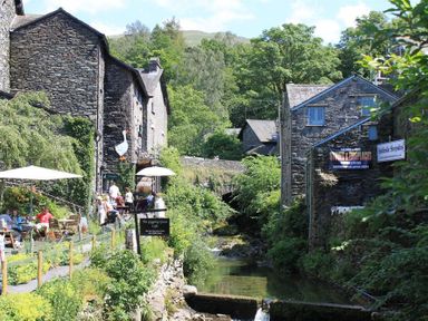 A riverside scene with stone buildings trees and outdoor seating at Acorn Cottage in Ambleside