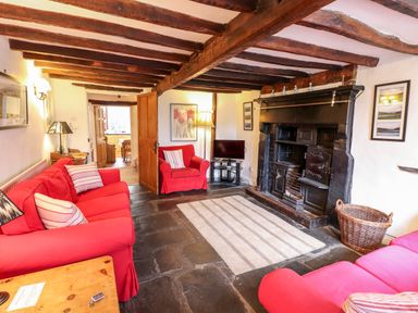 A living room with red sofas a rug and a large black fireplace at Rock Cottage in Ambleside