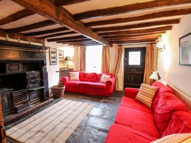 A living room with red sofas wooden ceiling beams a fireplace and a striped rug at Rock Cottage in Ambleside