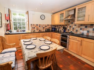 A kitchen with wooden cabinets a dining table set with plates and glasses and a window with wooden shutters at Rock Cottage in Ambleside