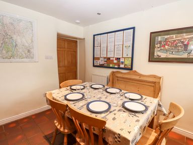 A dining table set with plates glasses and cutlery surrounded by wooden chairs and a bench in a room with a map and framed pictures on the walls at Rock Cottage Ambleside