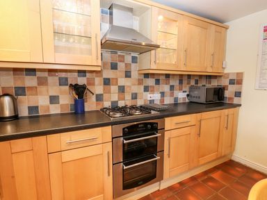 A kitchen with wooden cabinets a gas stove an oven a microwave a kettle and kitchen utensils at Rock Cottage in Ambleside