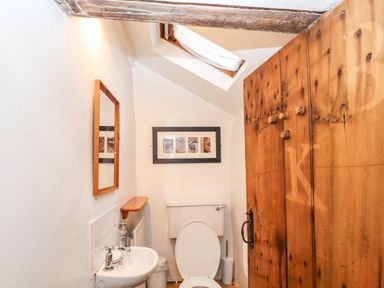 A small bathroom with a toilet sink wooden door mirror and skylight at Rock Cottage in Ambleside