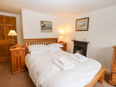 A bedroom with a double bed bedside tables lamps a fireplace and framed pictures at Rock Cottage in Ambleside