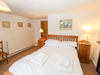 A bedroom with a double bed with white linens and wooden bedside tables with lamps at Rock Cottage in Ambleside