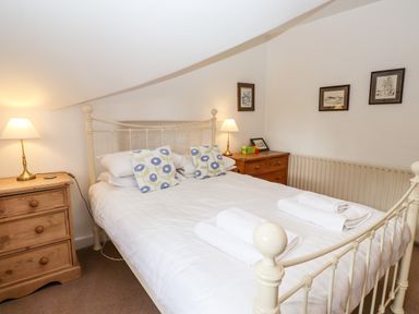 A bedroom with a double bed two wooden bedside tables with lamps and framed pictures on the wall at Rock Cottage Ambleside