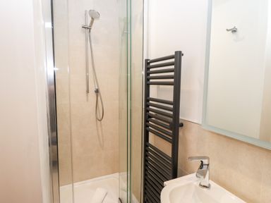A bathroom with a shower, black towel rail, sink with faucet, and a mirror at Rock Cottage in Ambleside