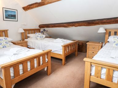A bedroom with three single wooden beds white bedding and wooden nightstands with lamps at Rock Cottage in Ambleside