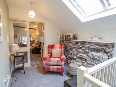 A seating area with a red armchair and plaid footstool next to a stone wall with books and ceramic ducks at Highfold in Ambleside