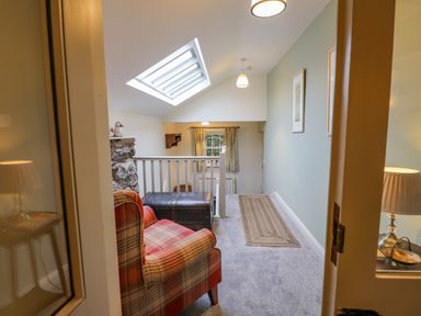 A hallway with a plaid armchair a wooden chest a skylight window and framed pictures on the wall at Highfold Ambleside