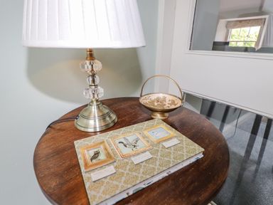A wooden table with a lamp a decorative book and a small bowl in a room with a window at Highfold in Ambleside