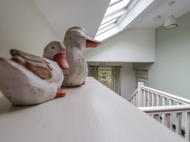 Two decorative duck sculptures on a ledge near a stairway with white railing and skylight at Highfold in Ambleside