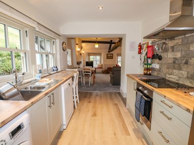 A kitchen with wooden countertops and white cabinets leading to a dining area with a table and chairs at Highfold in Ambleside