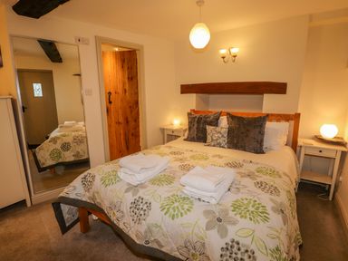 A bedroom with a double bed with floral bedding two bedside tables with lamps and a large mirror at Highfold in Ambleside
