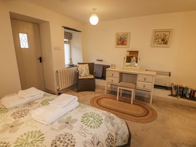 A bedroom with a bed with folded towels a dressing table a chair a window and a door at Highfold in Ambleside