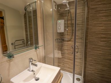 A bathroom with a sink and faucet a mirror a towel rack and a shower with glass doors and a wall-mounted shower unit at Highfold in Ambleside